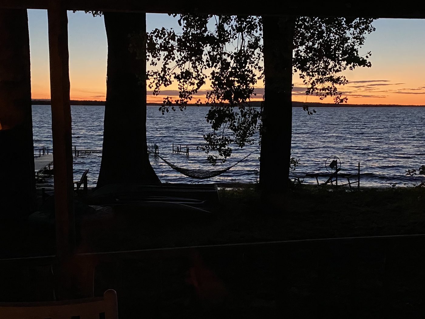 A hammock strung between trees above a lake at dusk